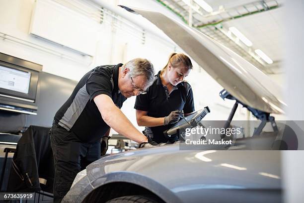 male and female technicians examining car at shop - hebebühne stock-fotos und bilder