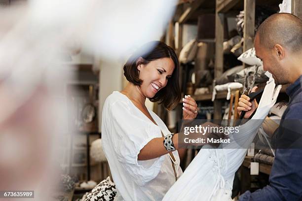 smiling female customer looking at white dress held by owner in store - clothing store stockfoto's en -beelden