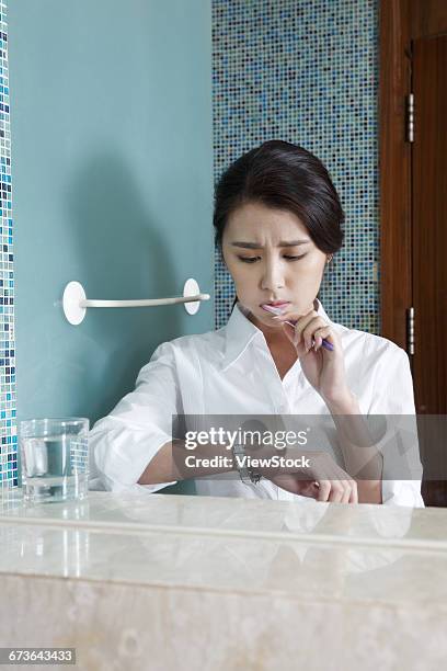young woman look at wrist watch while brushing her teeth - change toothbrush stock pictures, royalty-free photos & images