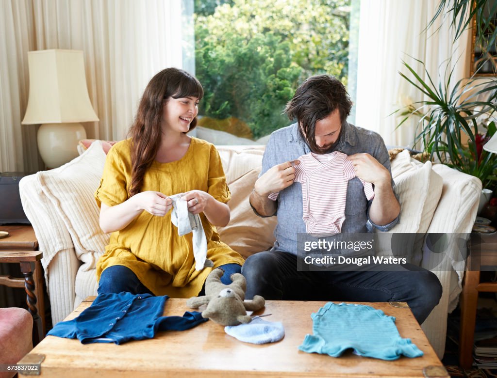 Pregnant couple looking at baby clothes at home.