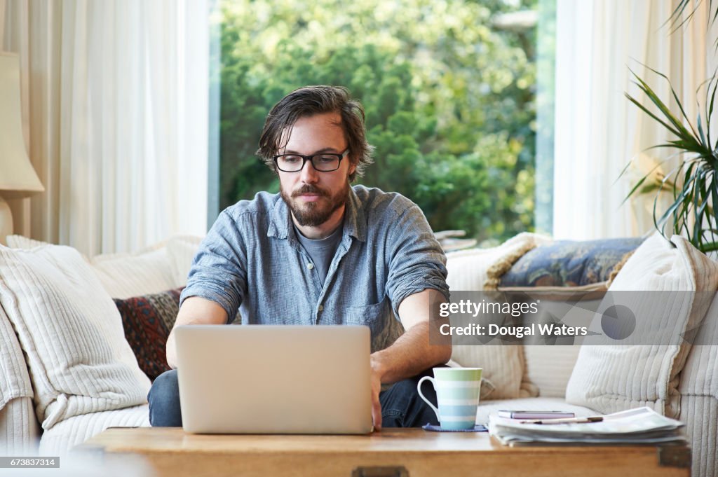 Man sitting on sofa and using laptop at home.