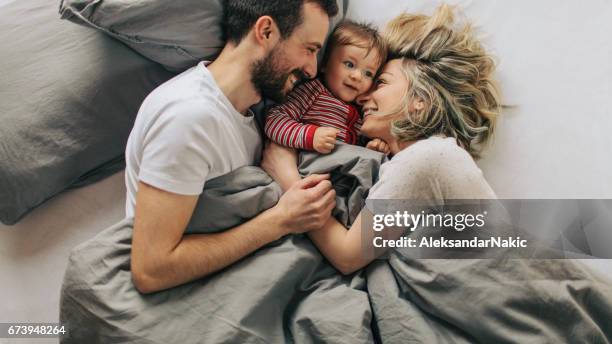 rutina de la mañana con nuestro bebé - pareja abrazados cama fotografías e imágenes de stock