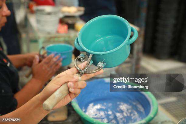 Employees coat pewter cookware with paint during the enamel process at the Baro Industrial SA manufacturing facility in the Azcapotzalco neighborhood...