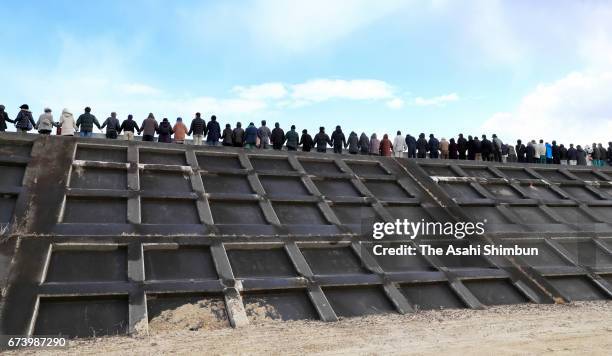 People hold their hands at 14:46, when the Magnitude 9.0 strong earthquake hit six years ago to commemorate the victims on a coastal levee in Taro...