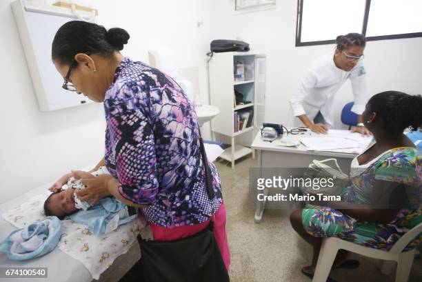 Dr. Êcaro Vidal dos Santos prepares to examine young patient Davi Luca as he is attended to by his grandmother Rita Cssia Guimares at the Posto Saude...