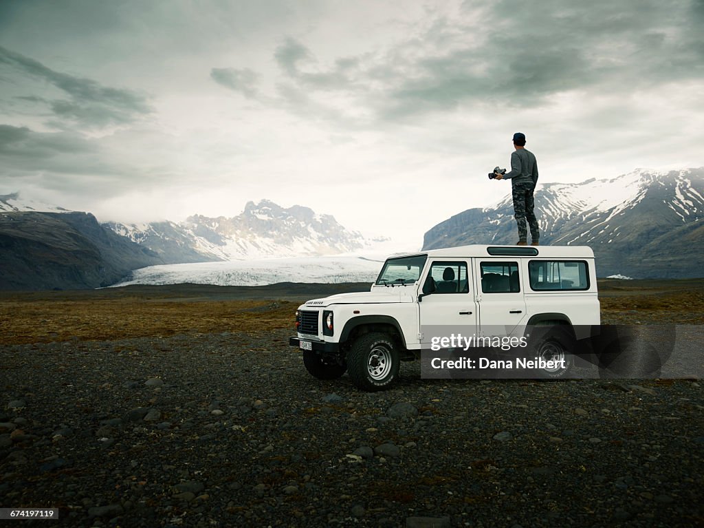Man taking pictures on top an off-road vehicle.