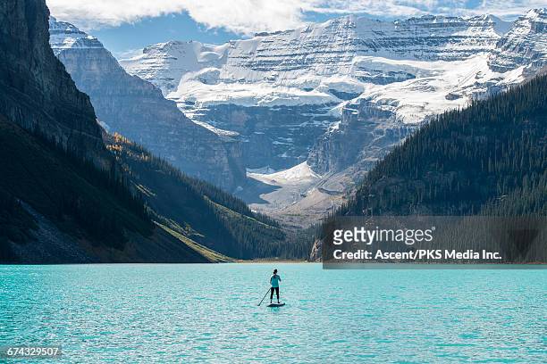 woman paddleboards across mountain lake - paddleboarding stock pictures, royalty-free photos & images