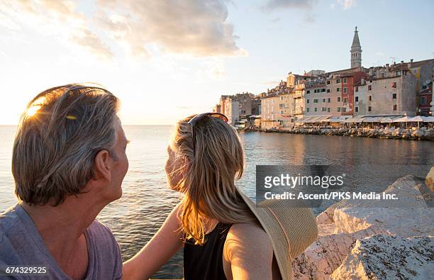 couple rest on rocks above sea, town behind - rovinj stock pictures, royalty-free photos & images
