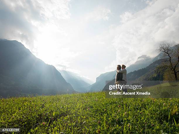 couple pause in meadow to watch sunrise on mtns - thinking man cloud stockfoto's en -beelden