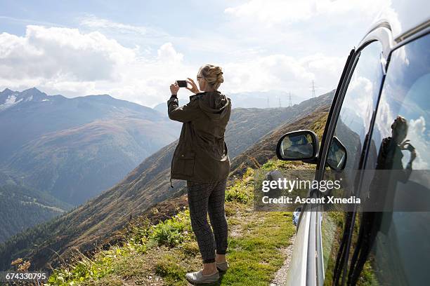 woman takes smart phone pic beside car, mtns - woman photographing stock pictures, royalty-free photos & images