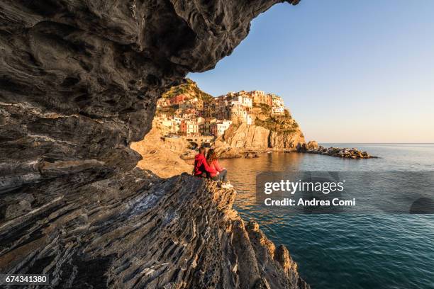 a young couple admiring the sunset from the rocks in manarola. manarola, cinque terre, la spezia, liguria. - unesco gruppo organizzato foto e immagini stock