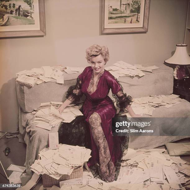 Marilyn Monroe , wearing a red negligee trimmed with black lace, sorts out her fan mail shortly after her film 'The Asphalt Jungle' had been...