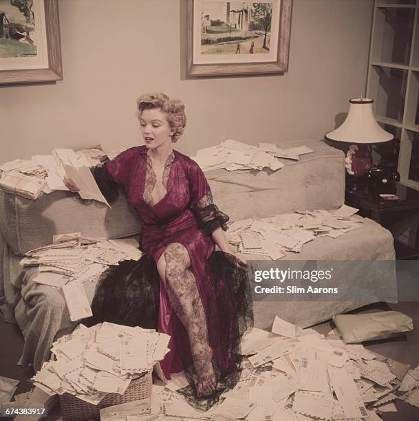 Marilyn Monroe , wearing a red negligee trimmed with black lace, sorts out her fan mail shortly after her film 'The Asphalt Jungle' had been...