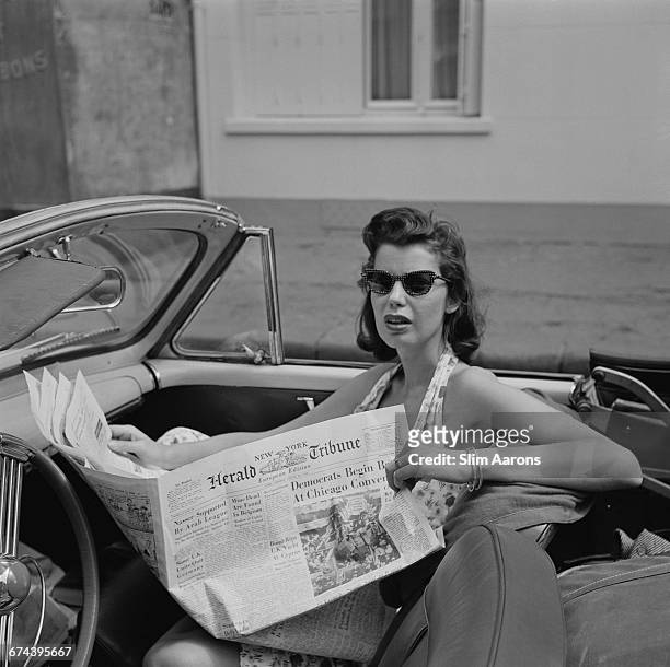 Rita Aarons, wife of photographer Slim Aarons, reading the European edition of the New York Herald Tribune newspaper in Monaco, 14th August 1956.