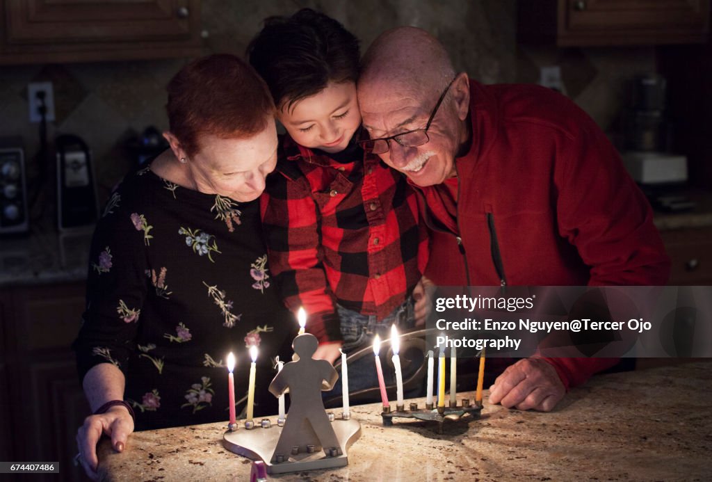 Judisk familj med granparents och sonson tända Hanukkah ljus i en menorah för semester