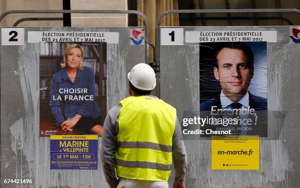 Worker looks at electoral posters of French presidential election candidate for the En Marche ! movement Emmanuel Macron and French presidential...