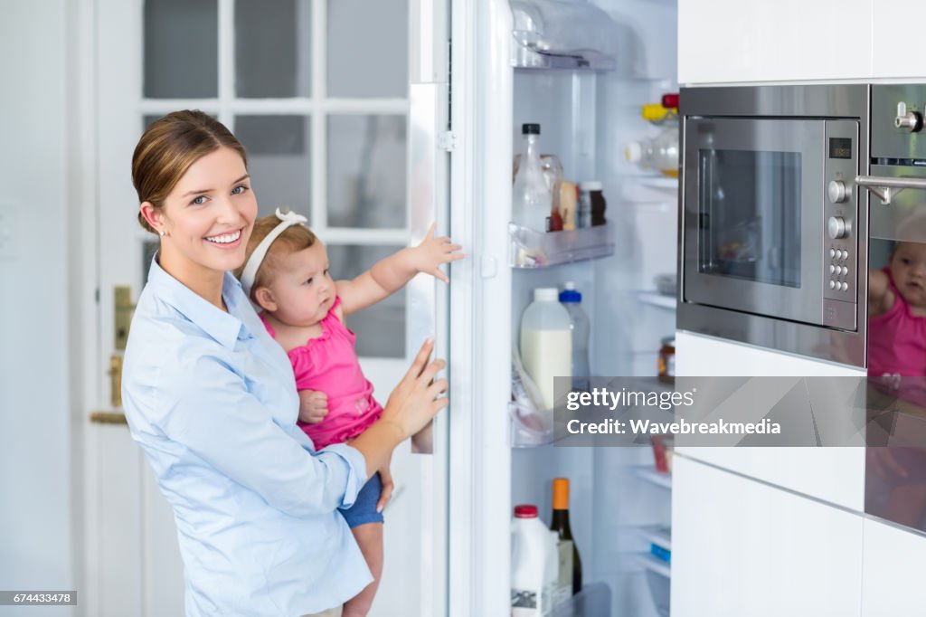 Frau Eröffnung Kühlschrank während des Tragens Babymädchen