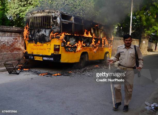 An Indian police official walkes near a burining bus , set by students , in Allahabad on April 2017. Allahabad University witnessed large scale...