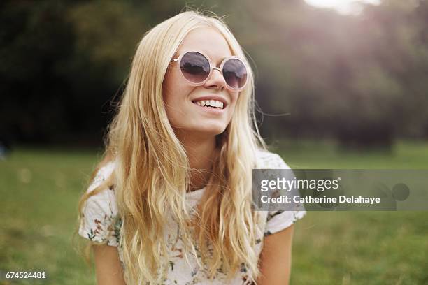 a blond young woman in a park - frau mit sonnenbrille stock-fotos und bilder