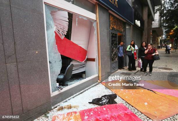 People view a bank window damaged by protestors during a nationwide general strike on April 28, 2017 in Rio de Janeiro, Brazil. The general strike...