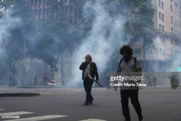 People walk past tear gas launched towards protestors by police during a nationwide general strike on April 28, 2017 in Rio de Janeiro, Brazil. The...