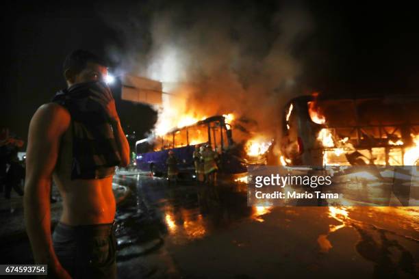 Man covers his faces as buses burn after being set on fire by protestors during a nationwide general strike on April 28, 2017 in Rio de Janeiro,...