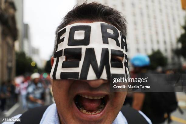 Protestor wears a mask, written in Portuguese, which means 'Temer Get Out' while marching at demonstrations during a nationwide general strike on...