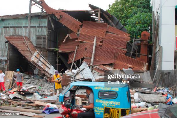 People stand next to debris from a collapsed house after a 6.8-magnitude earthquake hit General Santos City, in southern island of Mindanao on April...