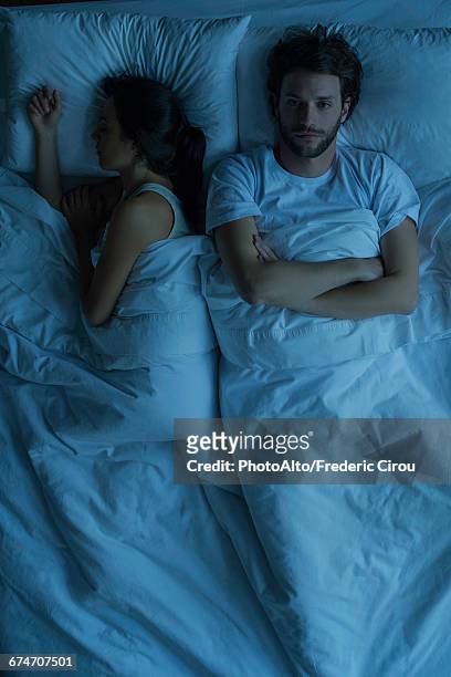 man lying awake in bed next to sleeping wife - insonia imagens e fotografias de stock