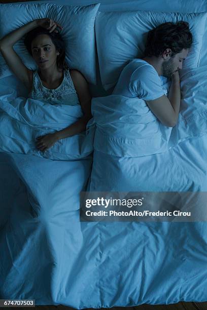 woman lying awake next to sleeping husband - above view of man sleeping on bed stock-fotos und bilder