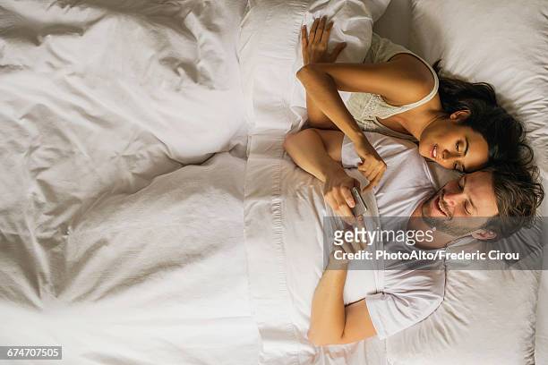 couple using smartphone together while lying in bed - instagram husband stock pictures, royalty-free photos & images