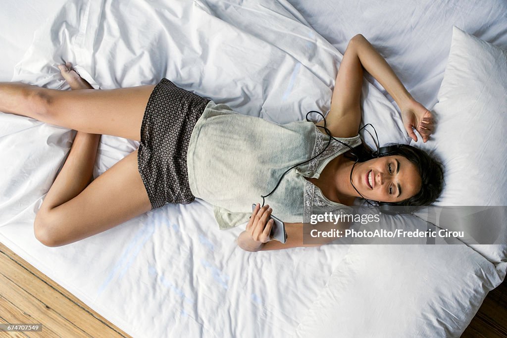 Woman lying on bed listening to music playing on smartphone