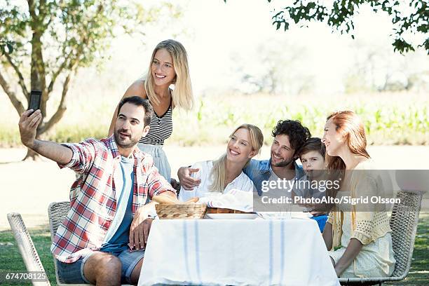 family posing for a group photo while picnicking outdoors - famiglia multimediale foto e immagini stock