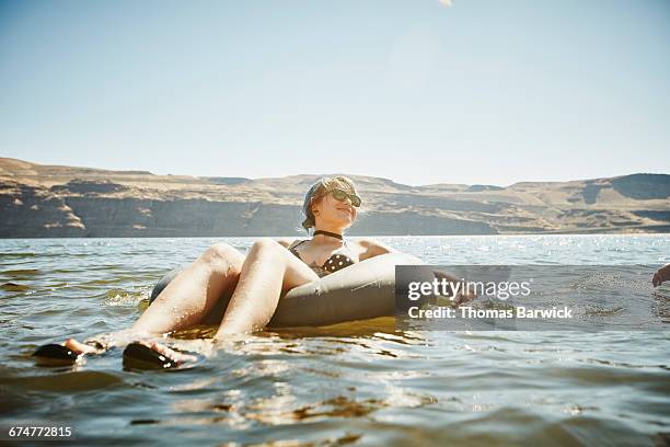 smiling woman floating in inner tube in river - 思い切って飛び込む ストックフォトと画像