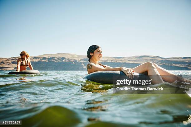 smiling women floating in inner tubes in river - floating on water stock pictures, royalty-free photos & images