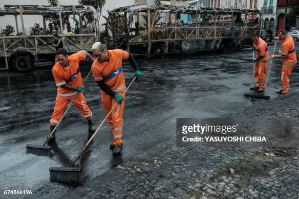 Sanitation workers clean the street where the night before buses were set on fire by protesters during the nationwide strike called by unions...