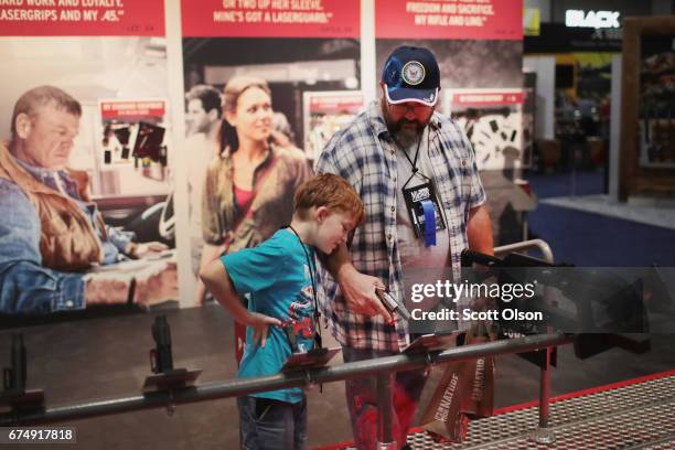 Andrew Farris and his son Eli look over guns fitted with Crimson-Trace sights at the 146th NRA Annual Meetings & Exhibits on April 29, 2017 in...