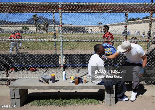 One inmate gives another a haircut while the San Quentin Athletics play against the Club Mexico team from Stockton, California, in the background on...