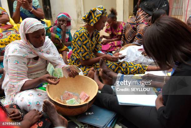 Binta Ndoye sits on a mat in a home in Grand-Mbao, on March 9 as she counts the money for a "cagnotte de la tontine" scheme, as members look on. The...