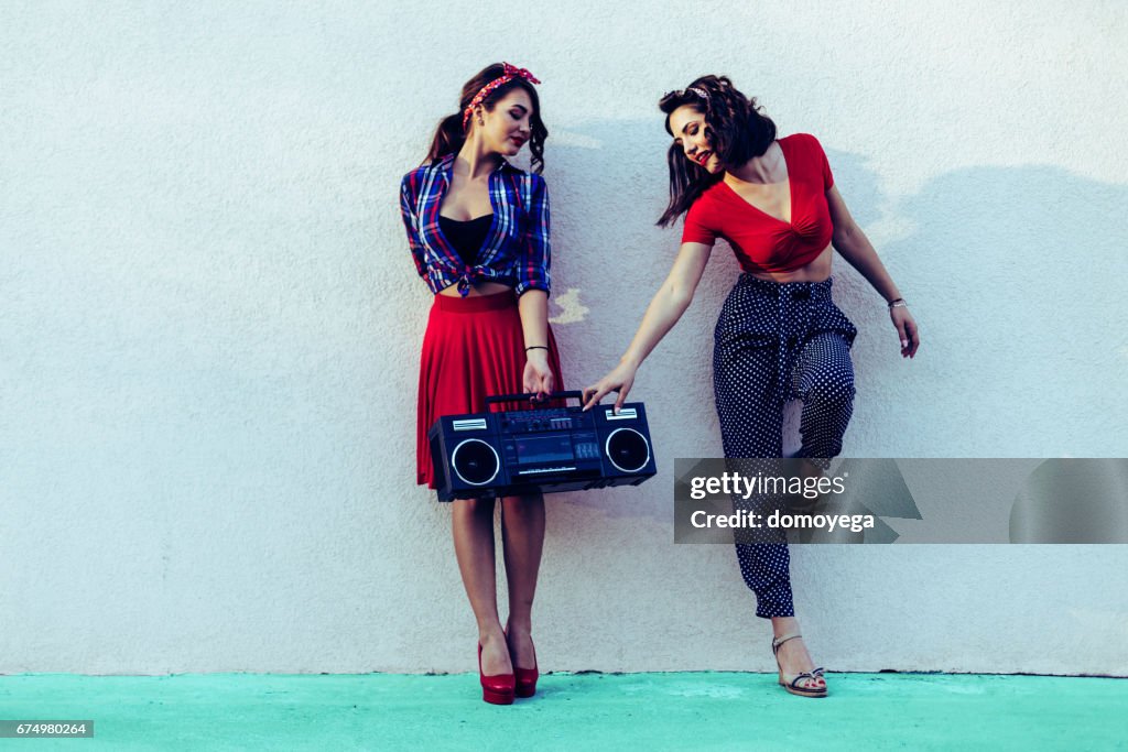 Beautiful pin-up girls leaning on the wall in the city street, carrying boom box