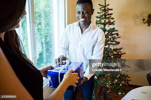 man handing over christmas present to woman - sala di lusso foto e immagini stock