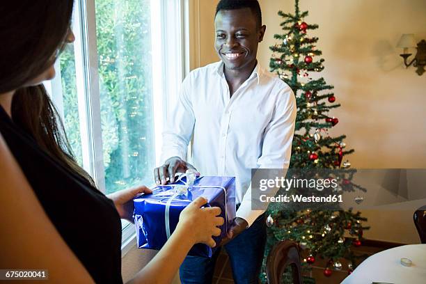 man handing over christmas present to woman - gift lounge stock pictures, royalty-free photos & images