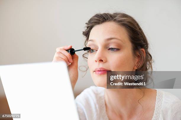 woman looking in mirror applying mascara - mascara stock pictures, royalty-free photos & images