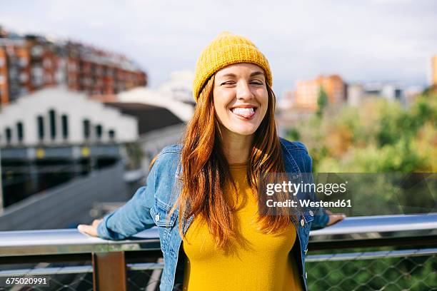 portrait of smiling young woman wearing yellow cap sticking out tongue - zwinkern stock-fotos und bilder