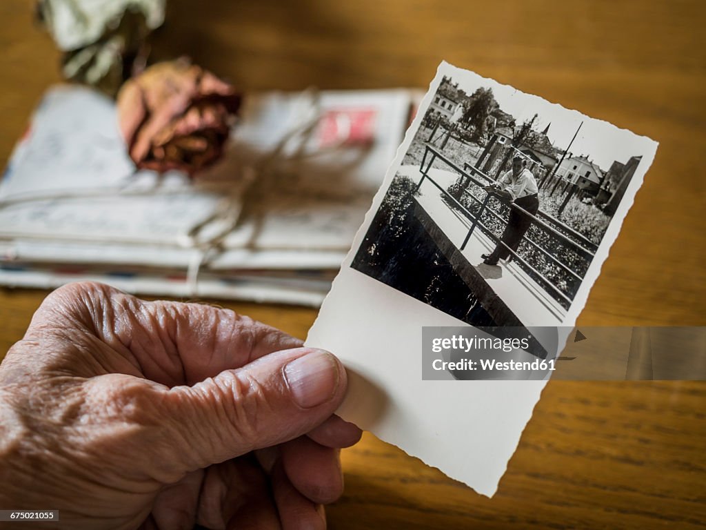 Old woman holding picture of her boyhood friend in hand, old letters and dried rose