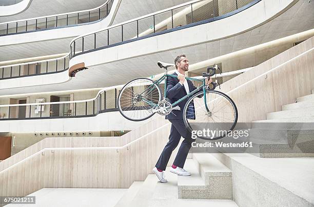 businesssman carrying bicycle in modern office building - carrying bike stock pictures, royalty-free photos & images