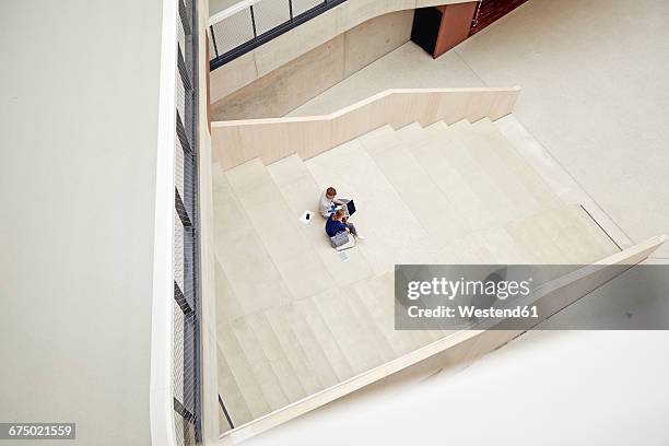 young man and woman sitting on staircase in a building using laptop - distant stock pictures, royalty-free photos & images
