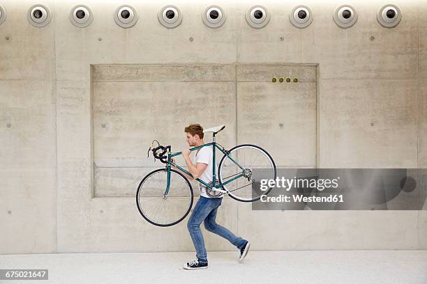 young man carrying bicycle on his shoulder in front of concrete wall - 肩に乗せる ストックフォトと画像