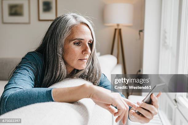 woman sitting on the couch looking at cell phone - one grey hair stock pictures, royalty-free photos & images