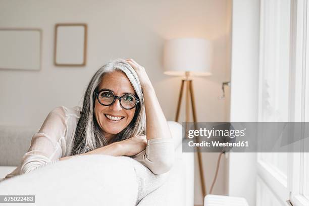 portrait of smiling woman sitting on the couch at home - einzelne frau über 40 stock-fotos und bilder